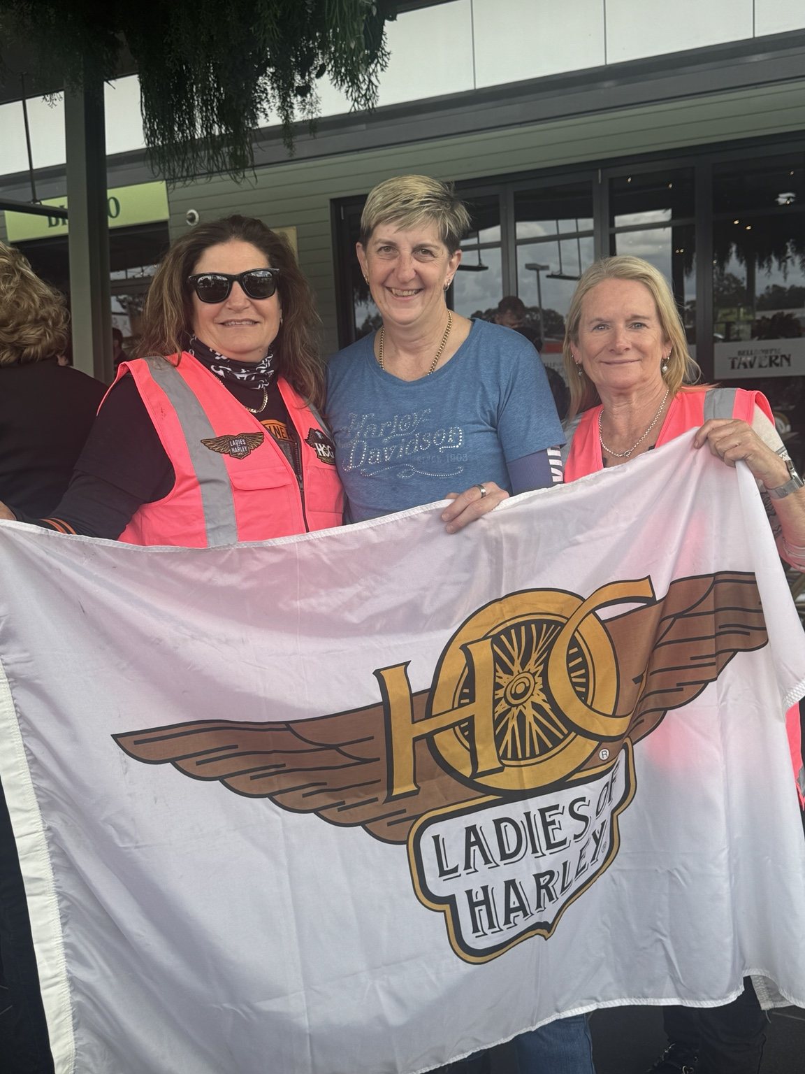 Three Ladies of Harley members holding the LOH flag